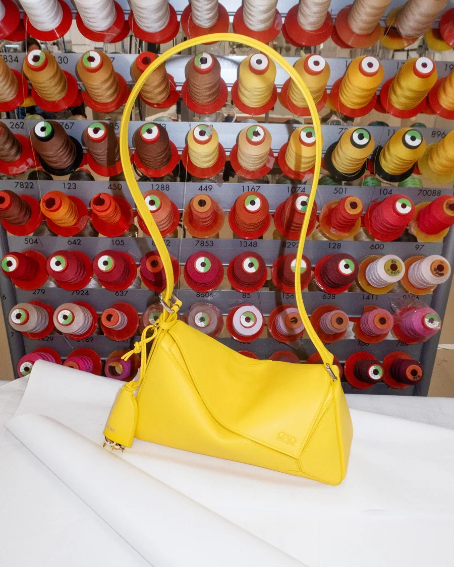 Making-of Loewe: eine gelbe Tasche in der Werkstatt vor einer Wand aus Garnspulen