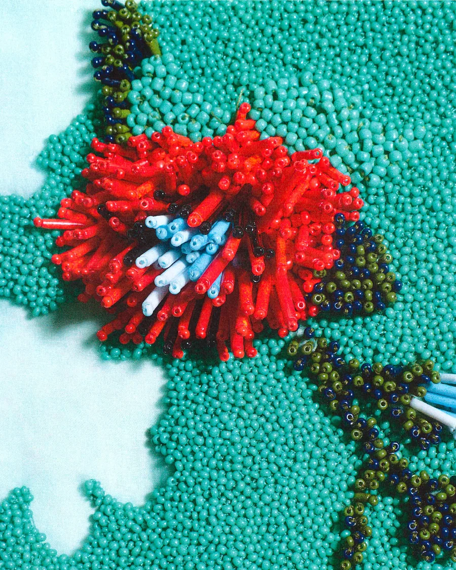 Making-of Loewe Frühjahr-Sommer 2027: eine rote Blüte aus Glasperlen gestickt auf türkisem Grund